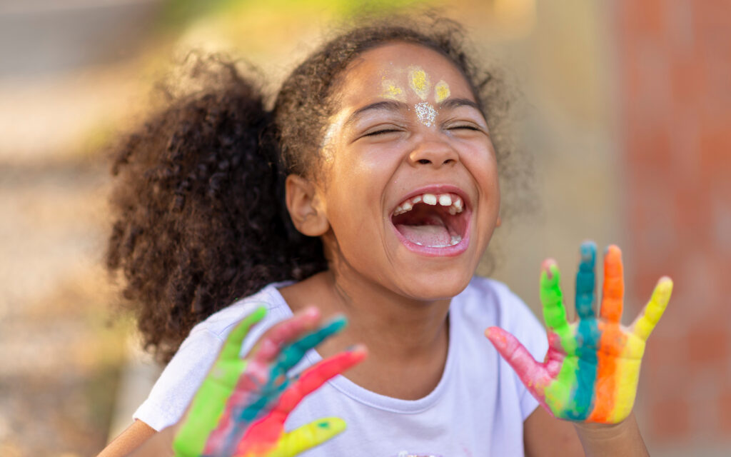 Girl with paint on her hands smiling.