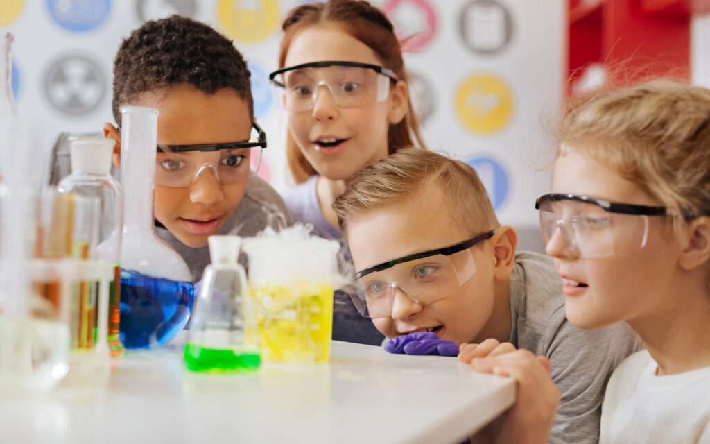 A group of kids with safety glasses on looking a science experiment.