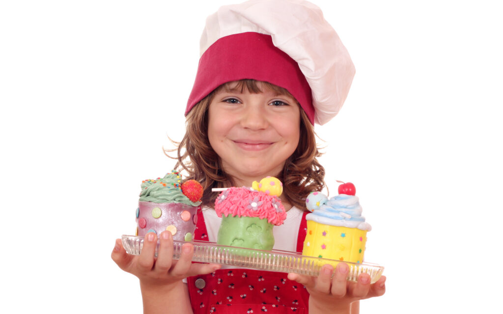 Girl wearing a chefs hat holding desserts.